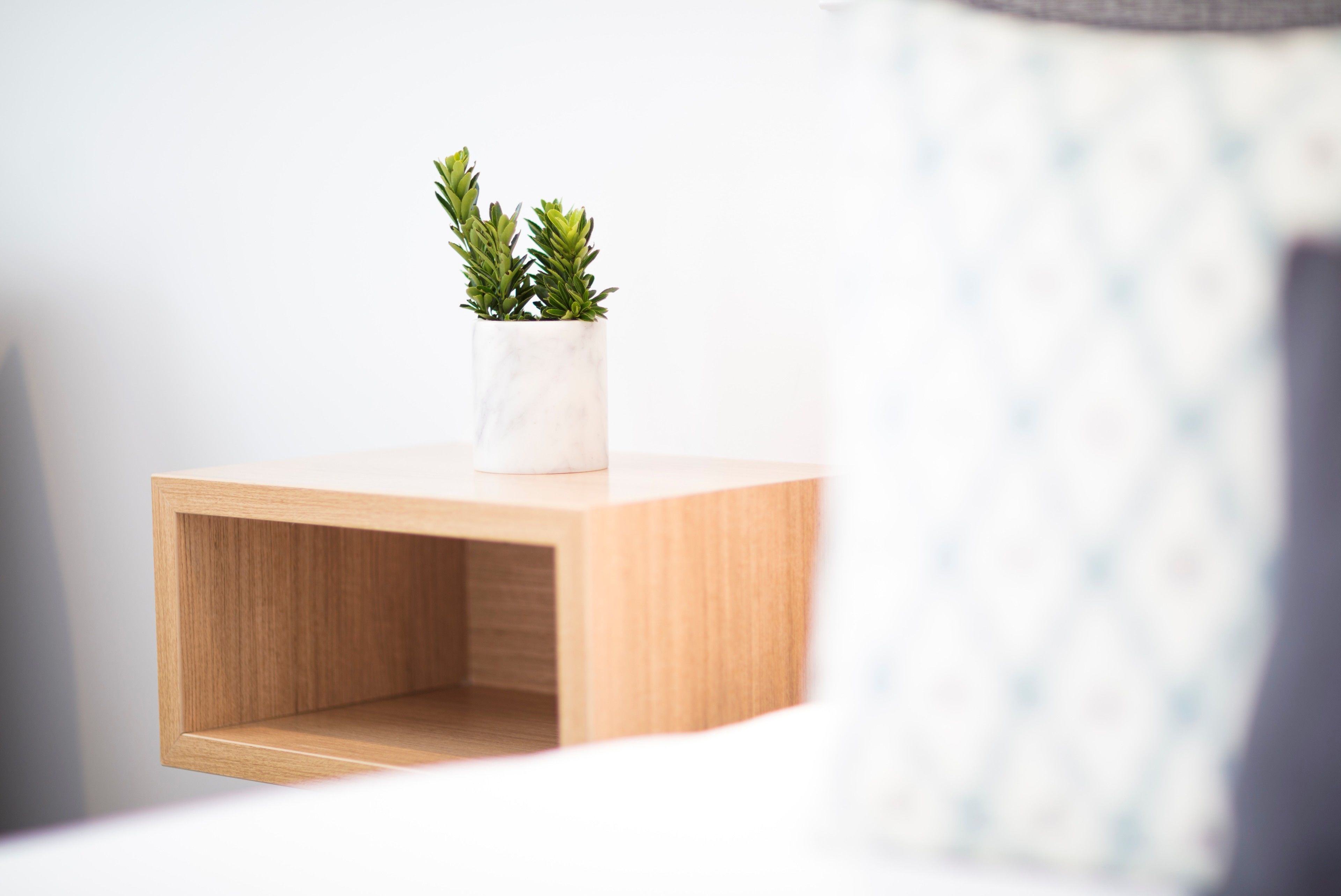 Una mesita de noche de madera con un jarrón blanco que contiene plantas verdes.
