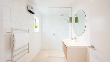 A modern bathroom with a glass shower enclosure, a towel rack, a sink with a mirror, and a small window with a plant.