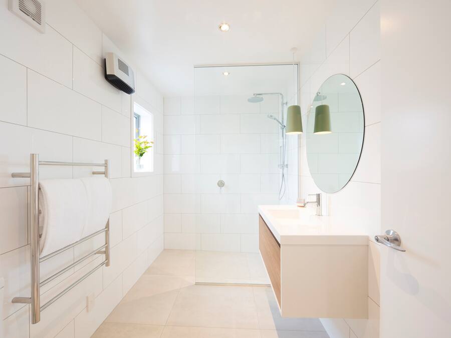 A modern bathroom with a glass shower enclosure, a towel rack, a sink with a mirror, and a small window with a plant.