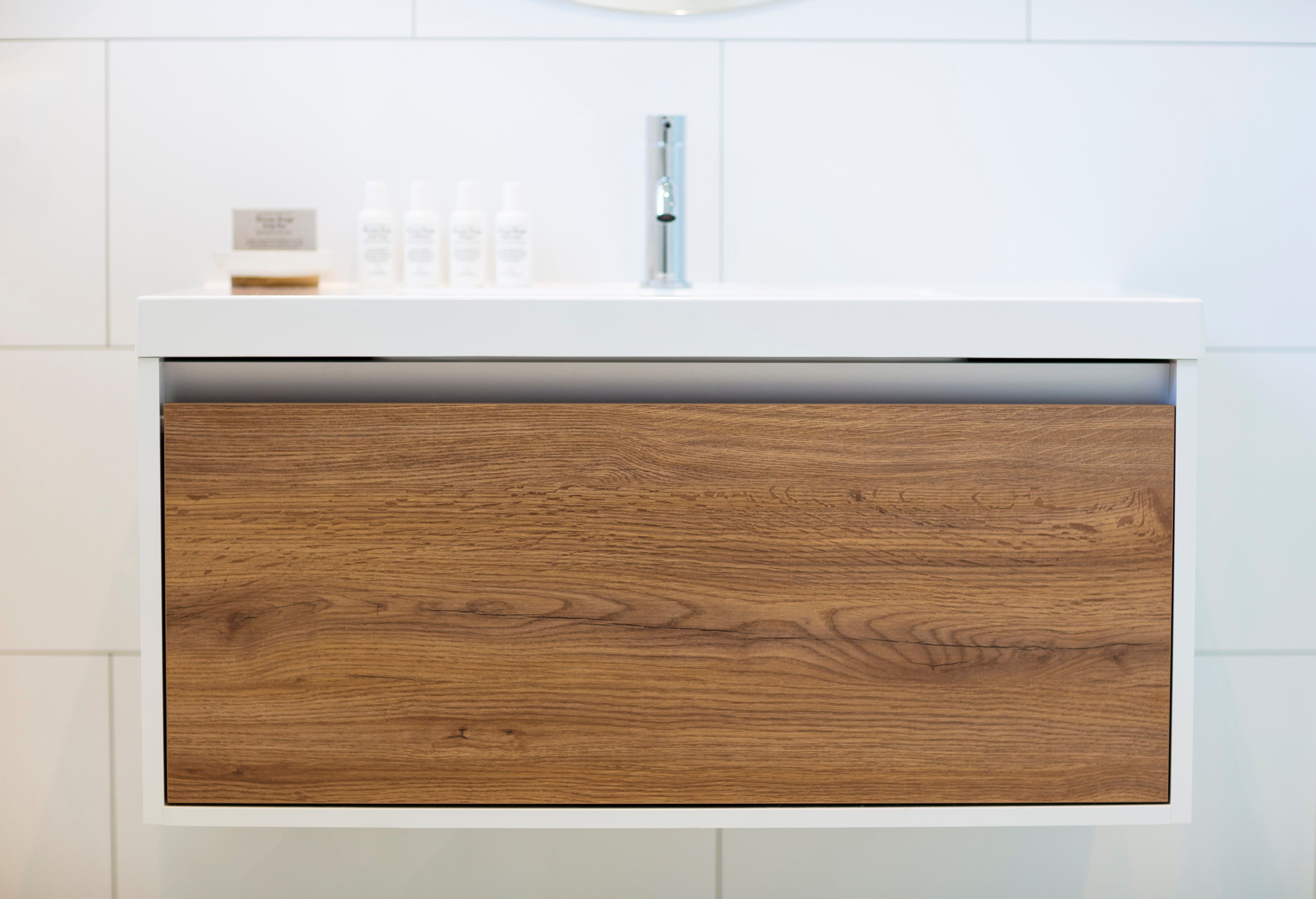 Une salle de bain moderne avec un lavabo blanc, un meuble en bois et des articles de toilette posés sur le comptoir.