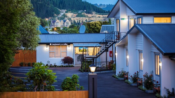 A hotel with a modern design, featuring a central staircase, a parking area, and a view of a forested hillside. - Beechwood Boutique Accommodation (Dunedin)