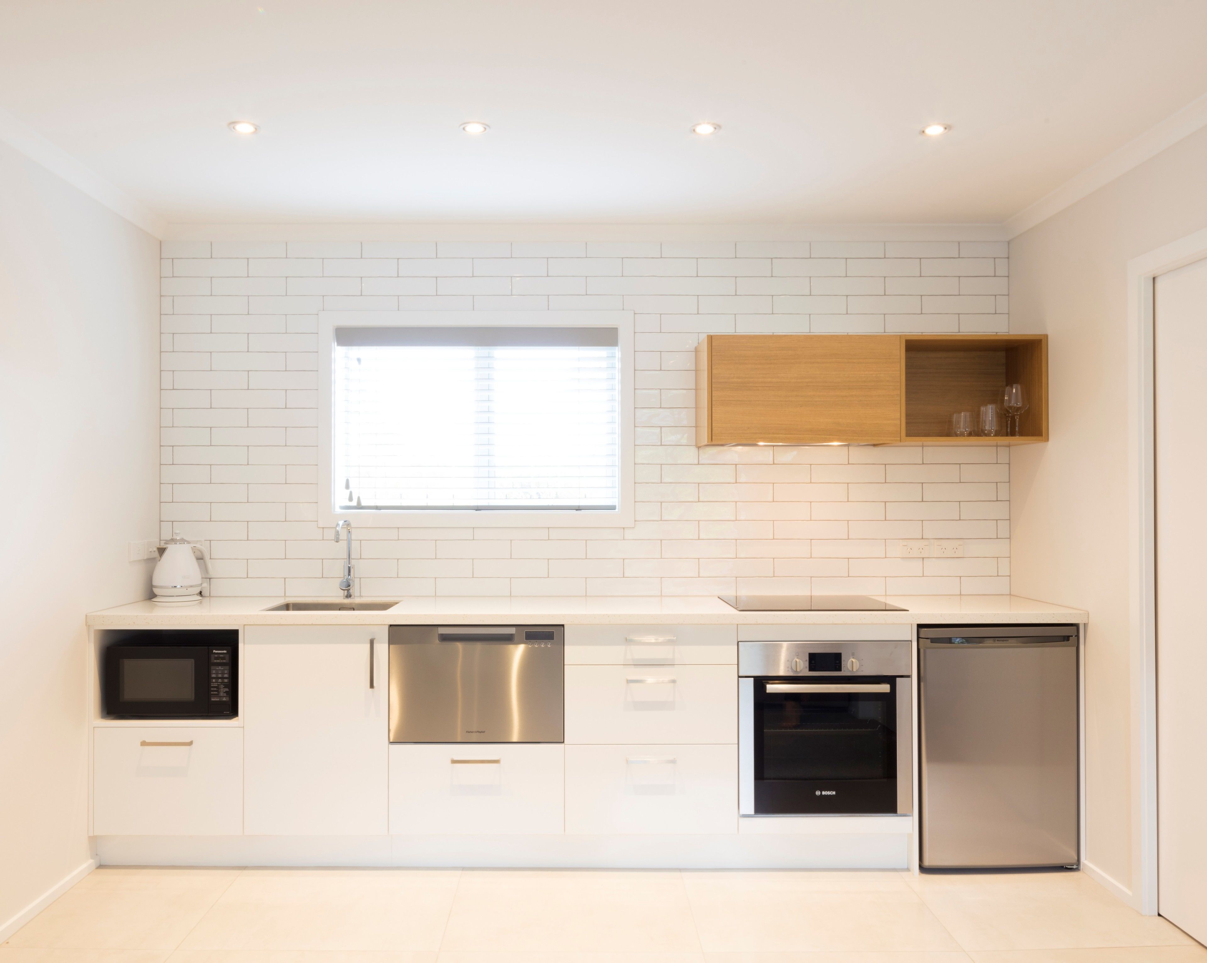 A modern kitchen with white subway tiles, stainless steel appliances, and a wooden upper cabinet.