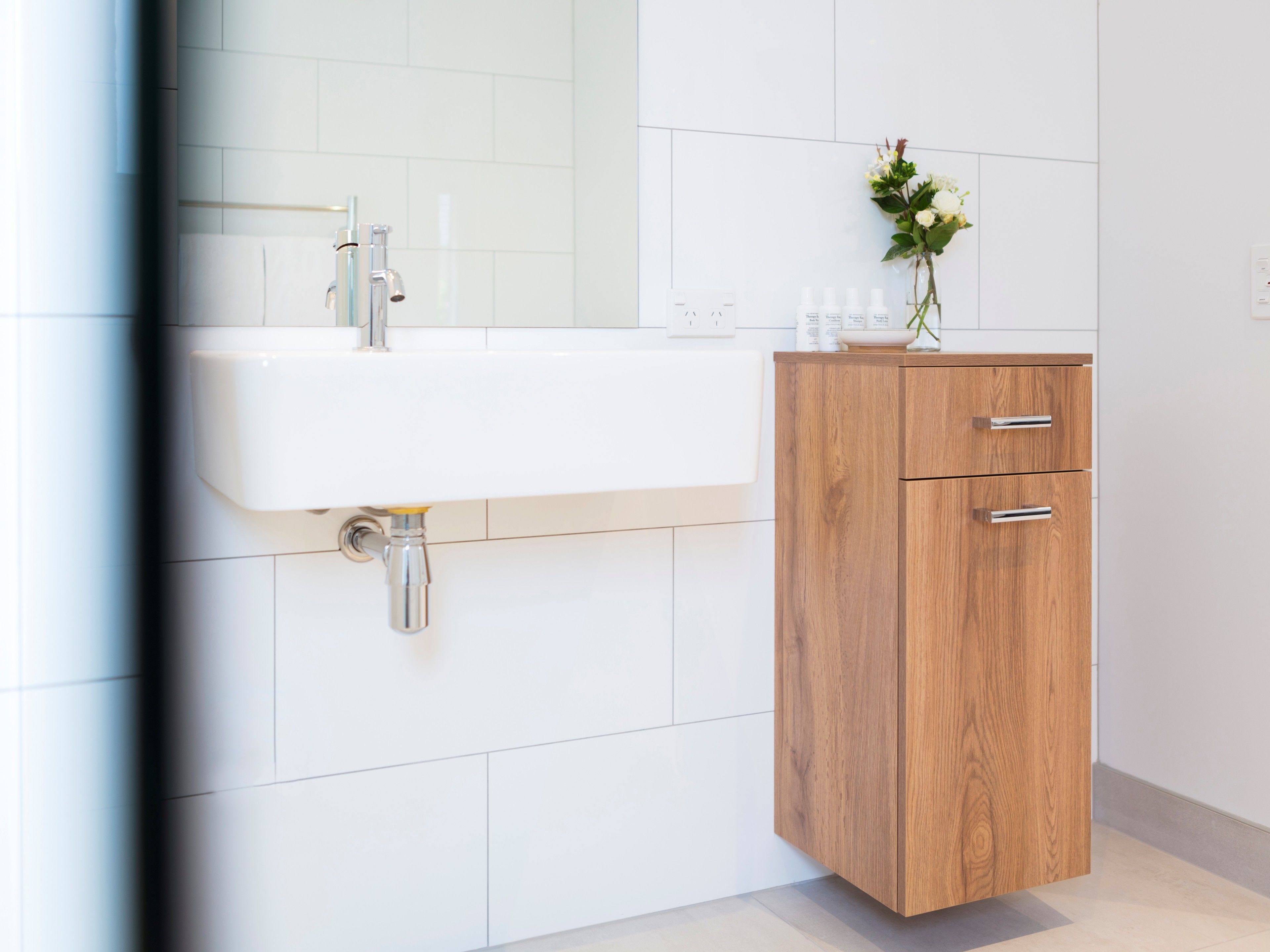 A modern bathroom with a white sink, wooden cabinet, and a mirror.