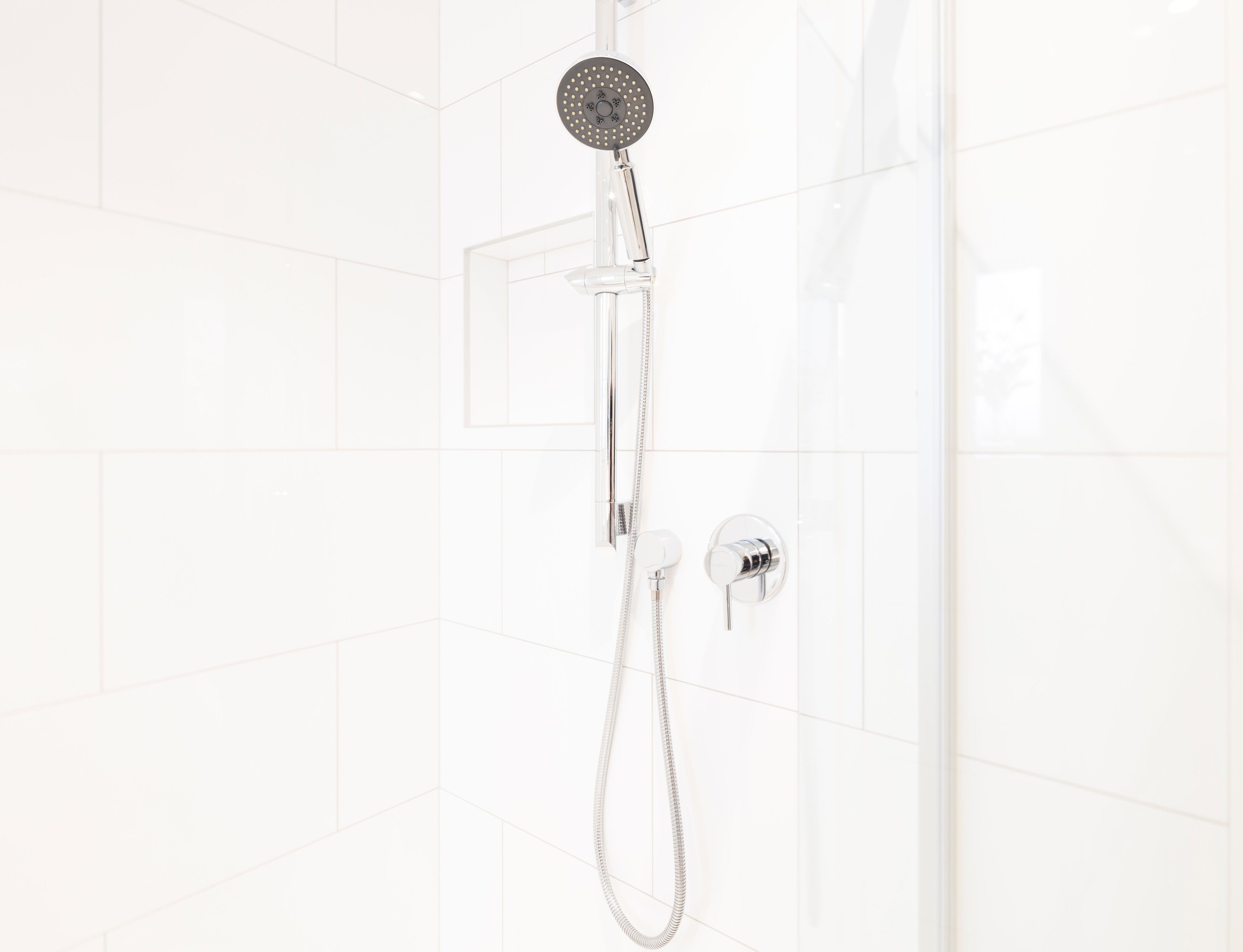 A shower with a handheld showerhead and a wall-mounted control.