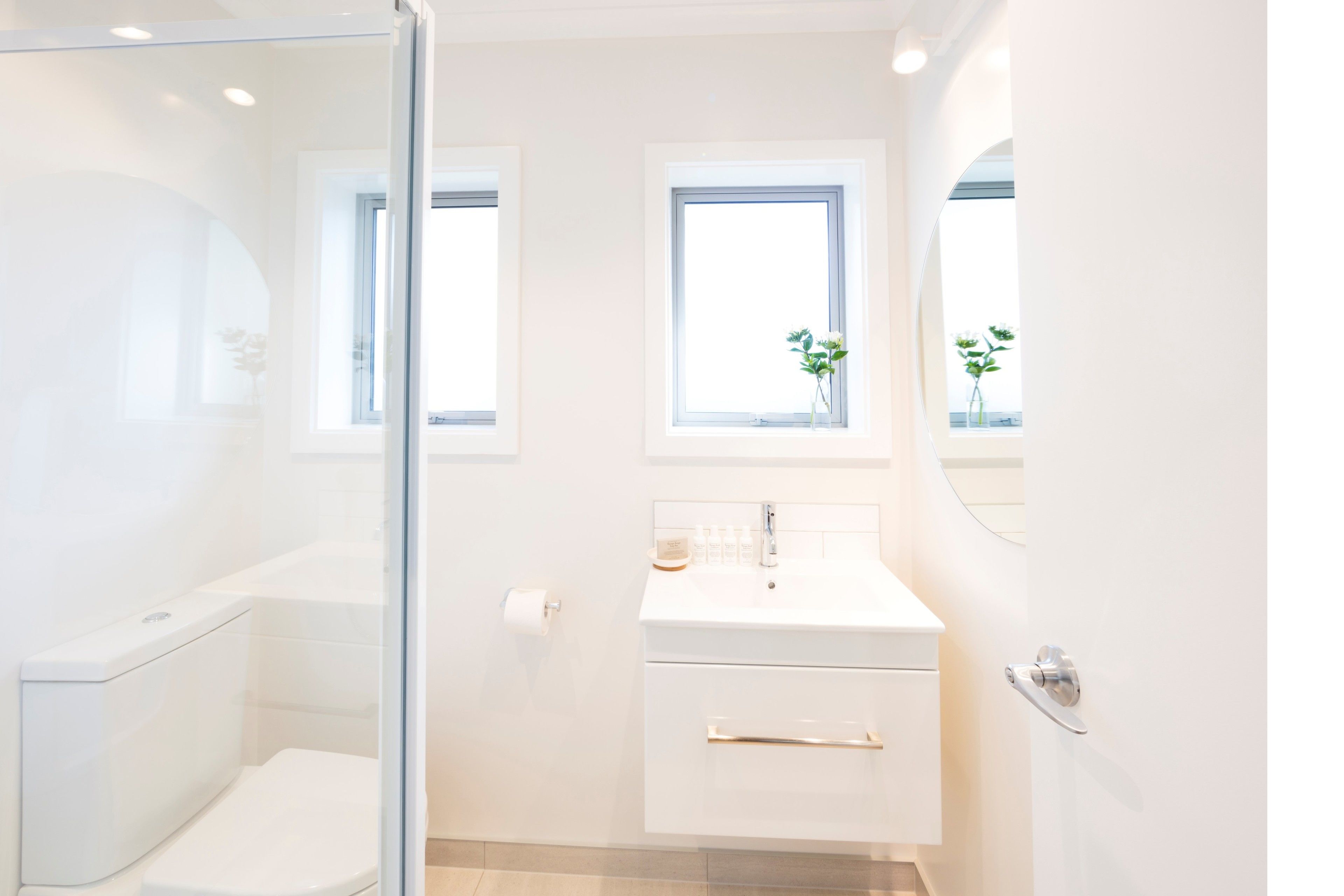 Un baño moderno con cabina de ducha de vidrio, un lavamanos blanco y un ventanal con vistas a zonas verdes.