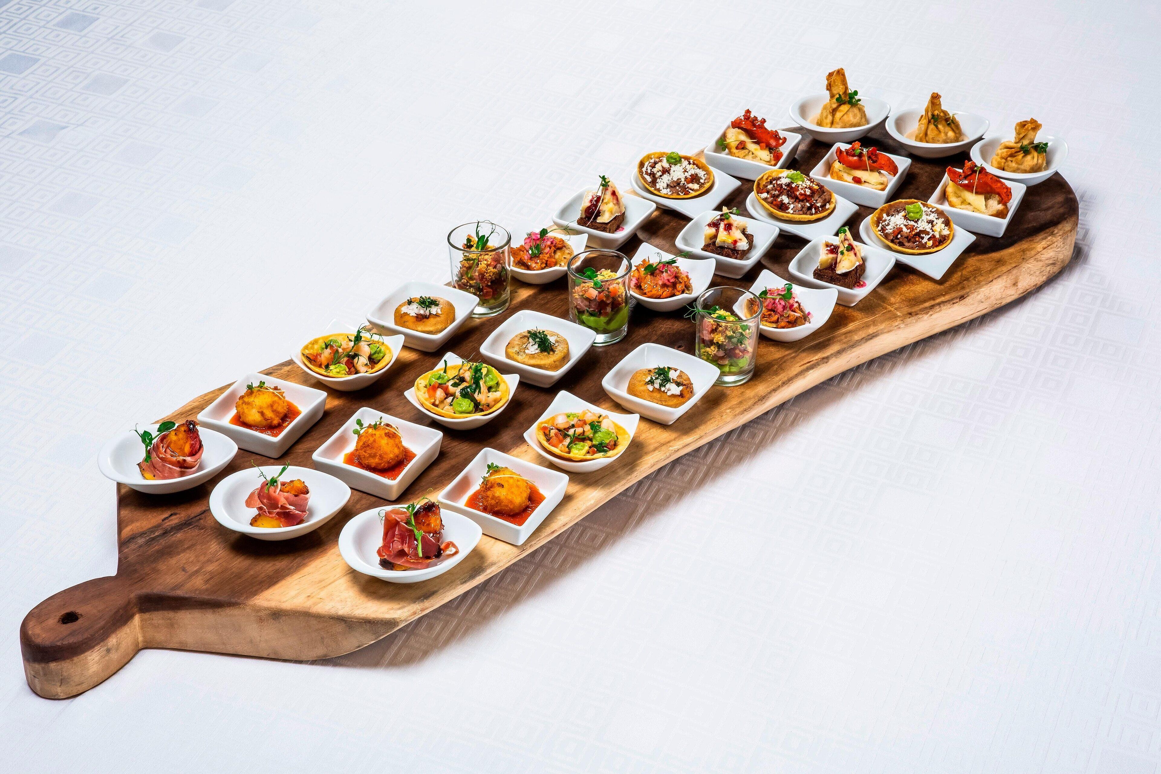 A wooden serving board with various small dishes of food arranged in a line.