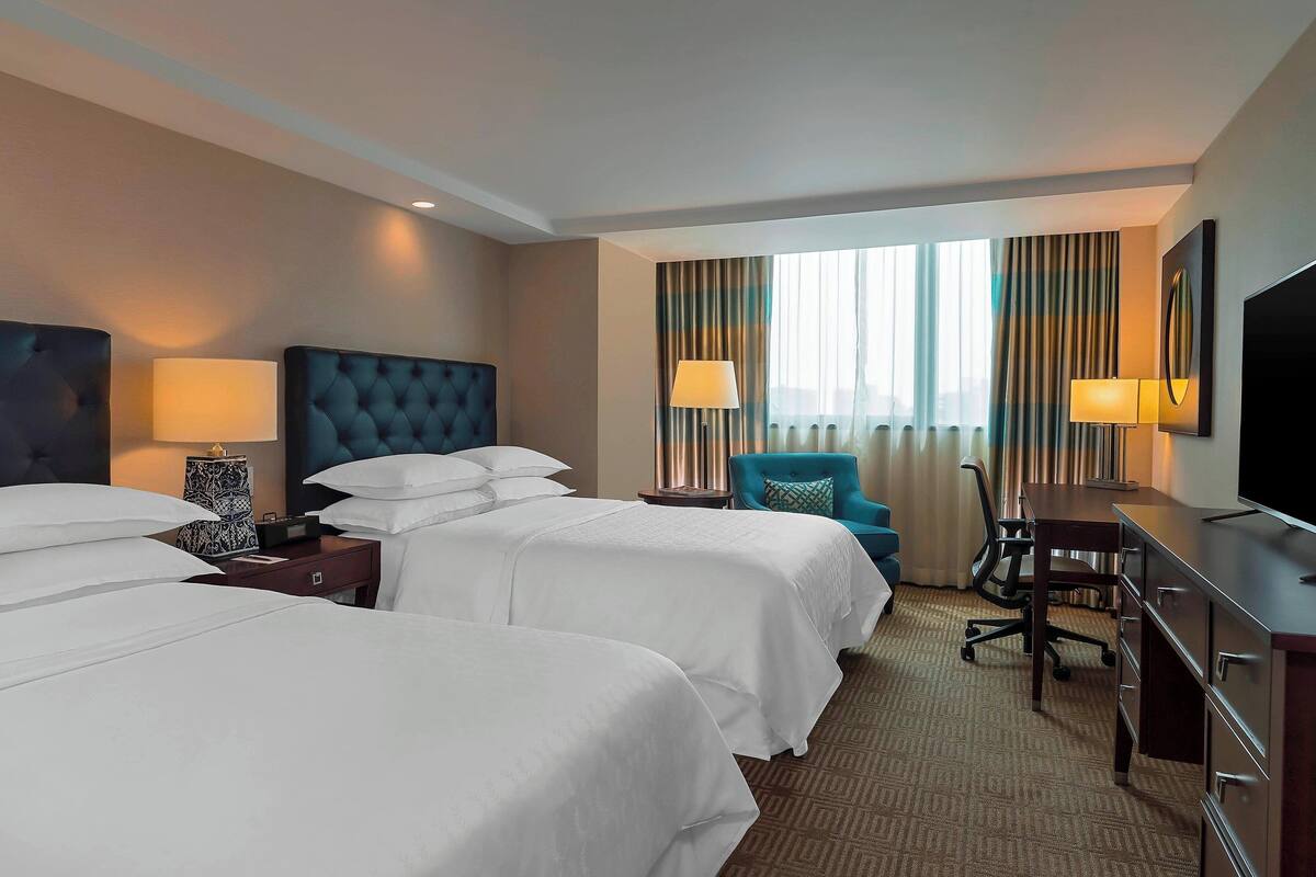 A hotel room with two beds, a desk, a chair, and a TV.