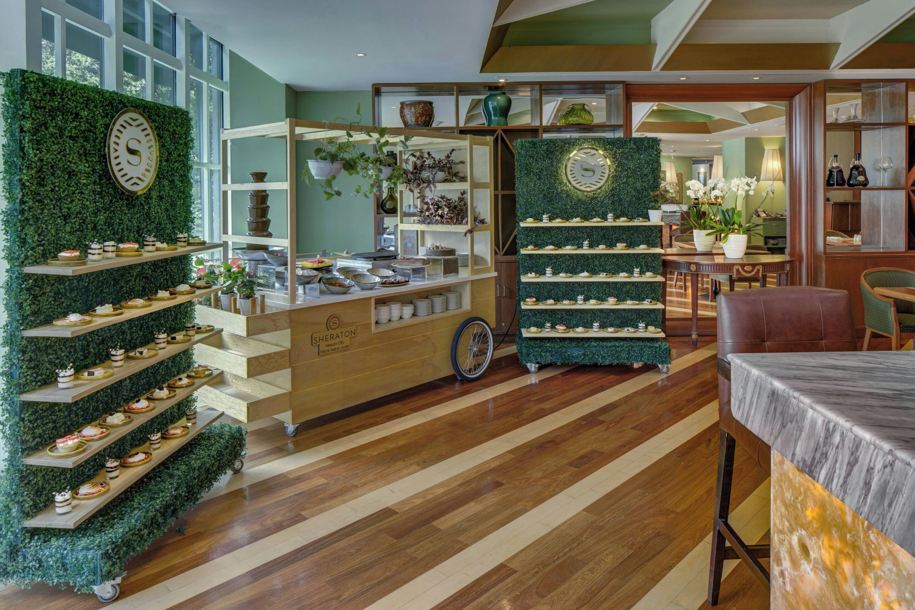 Um saguão de hotel com parede verde, balcão de recepção e área de estar com mesa e cadeiras.