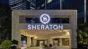 The Sheraton hotel entrance with a modern design, featuring a prominent illuminated logo and a well-lit facade.