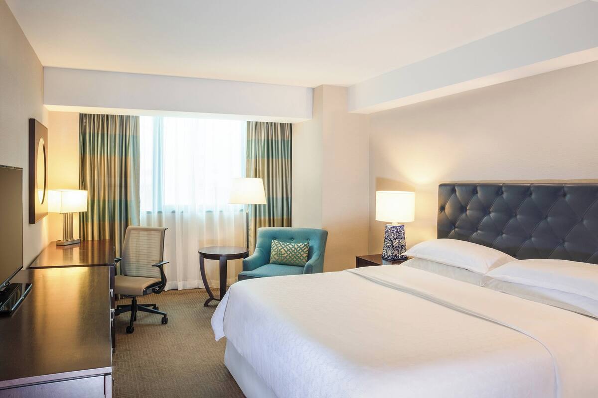 A hotel room with a bed, a desk, a chair, and a TV.
