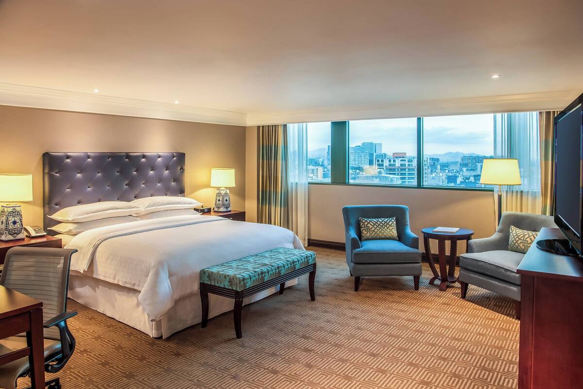 Una habitación de hotel con una cama grande, un escritorio, una silla, una mesita y un televisor.