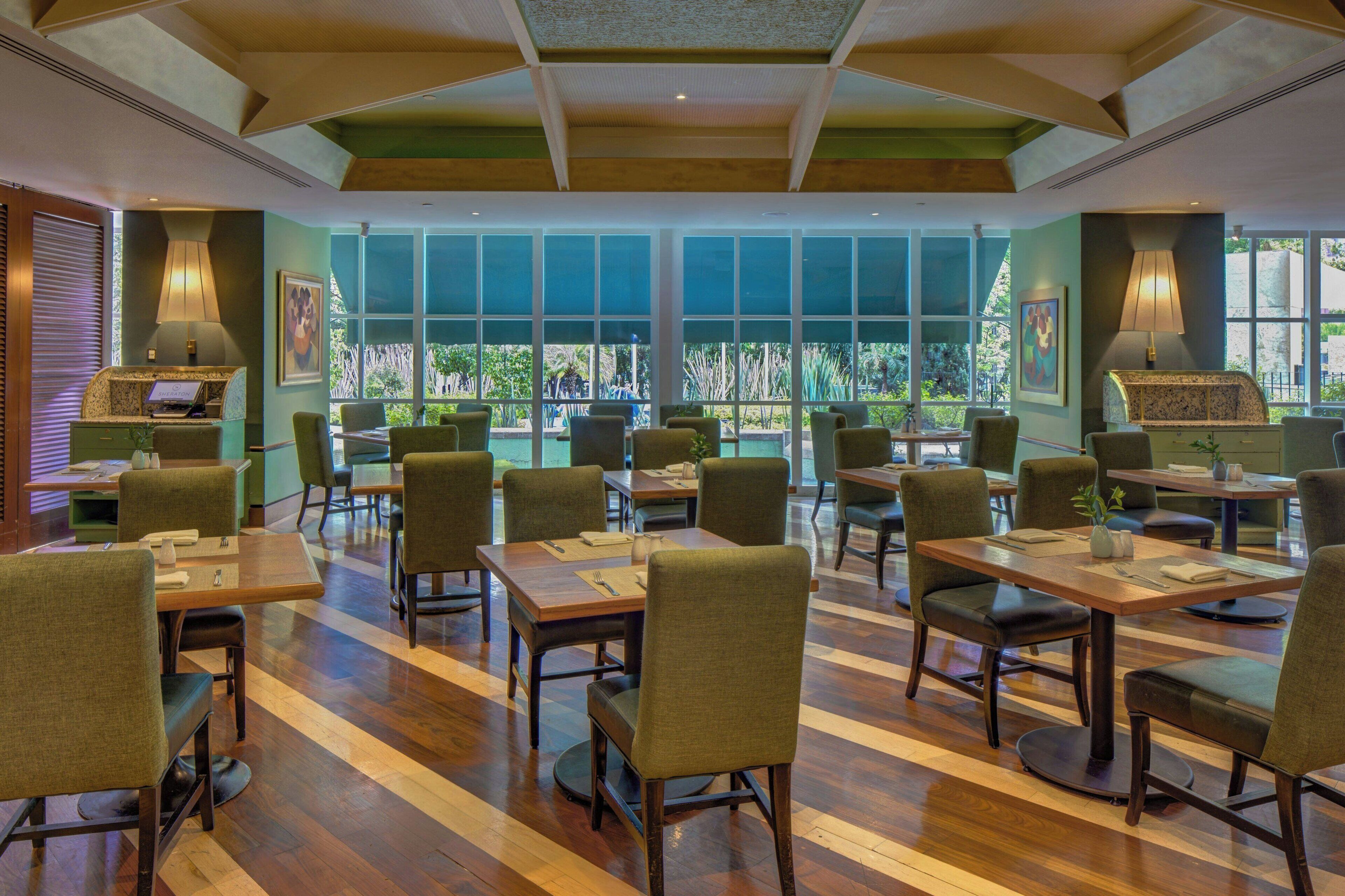 A restaurant with wooden tables and chairs, large windows, and green walls.