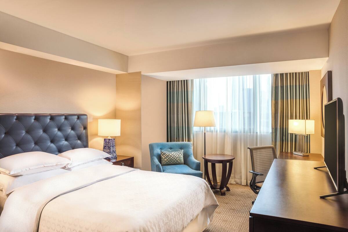 A hotel room with a large bed, two chairs, a desk, and a TV.