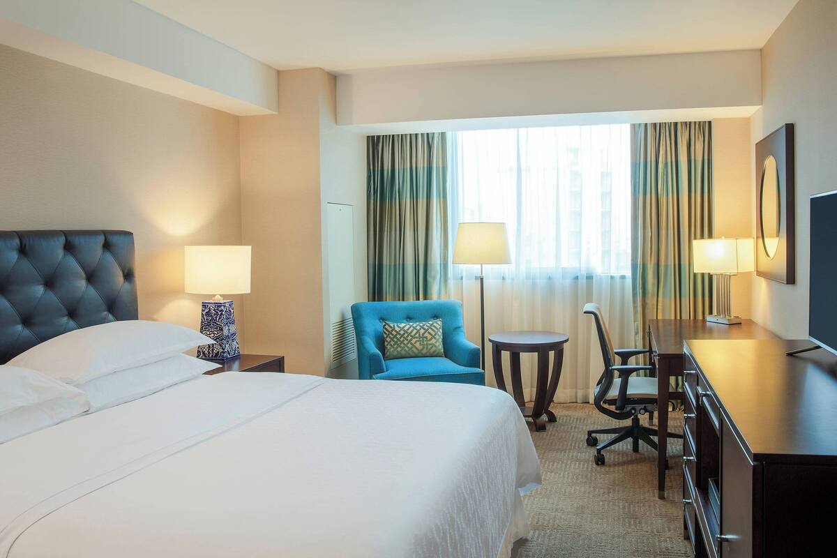 Una habitación de hotel con una cama grande, un sillón azul, un escritorio y un televisor.