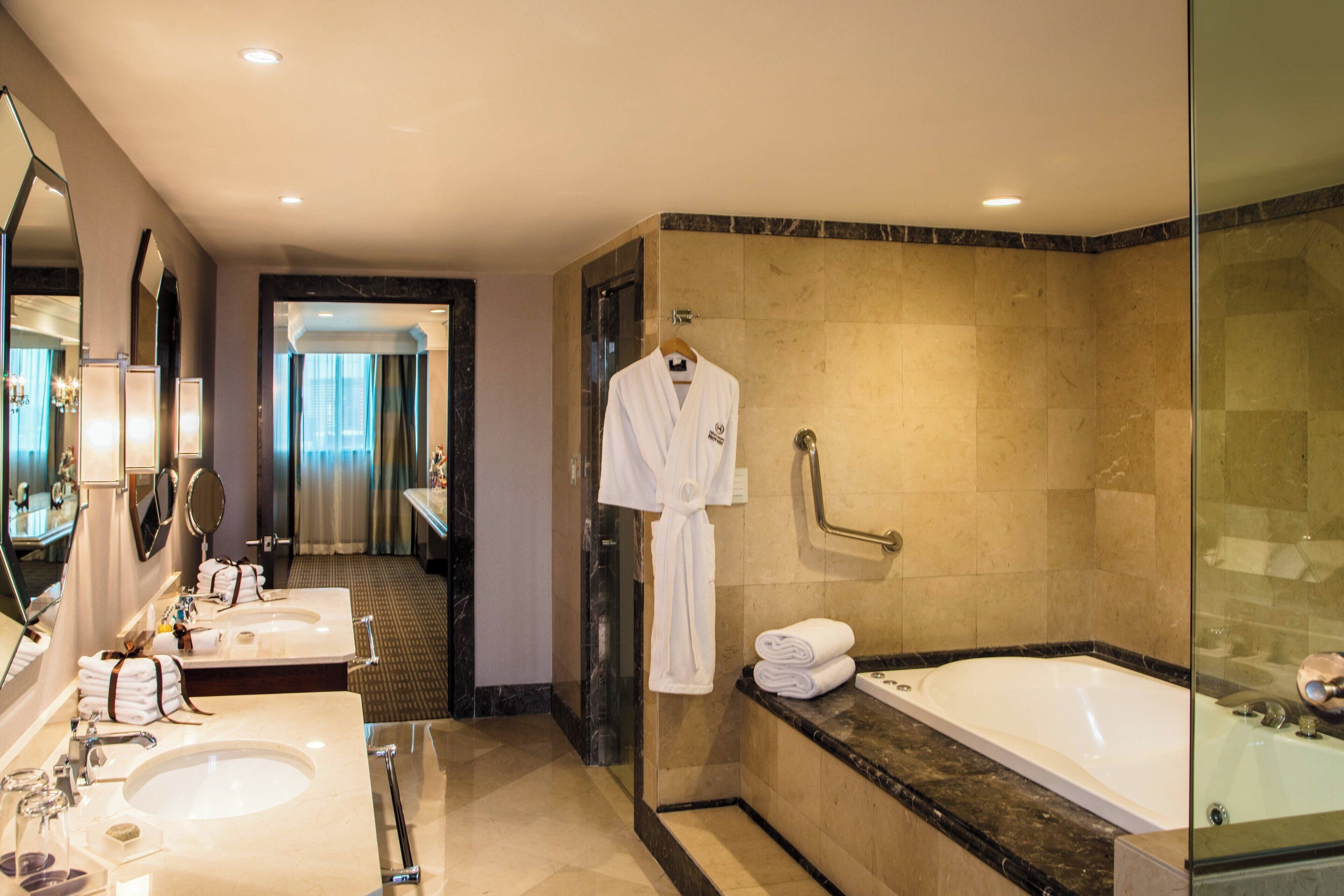 A hotel bathroom with two sinks, a bathtub, and a robe hanging on a rack.