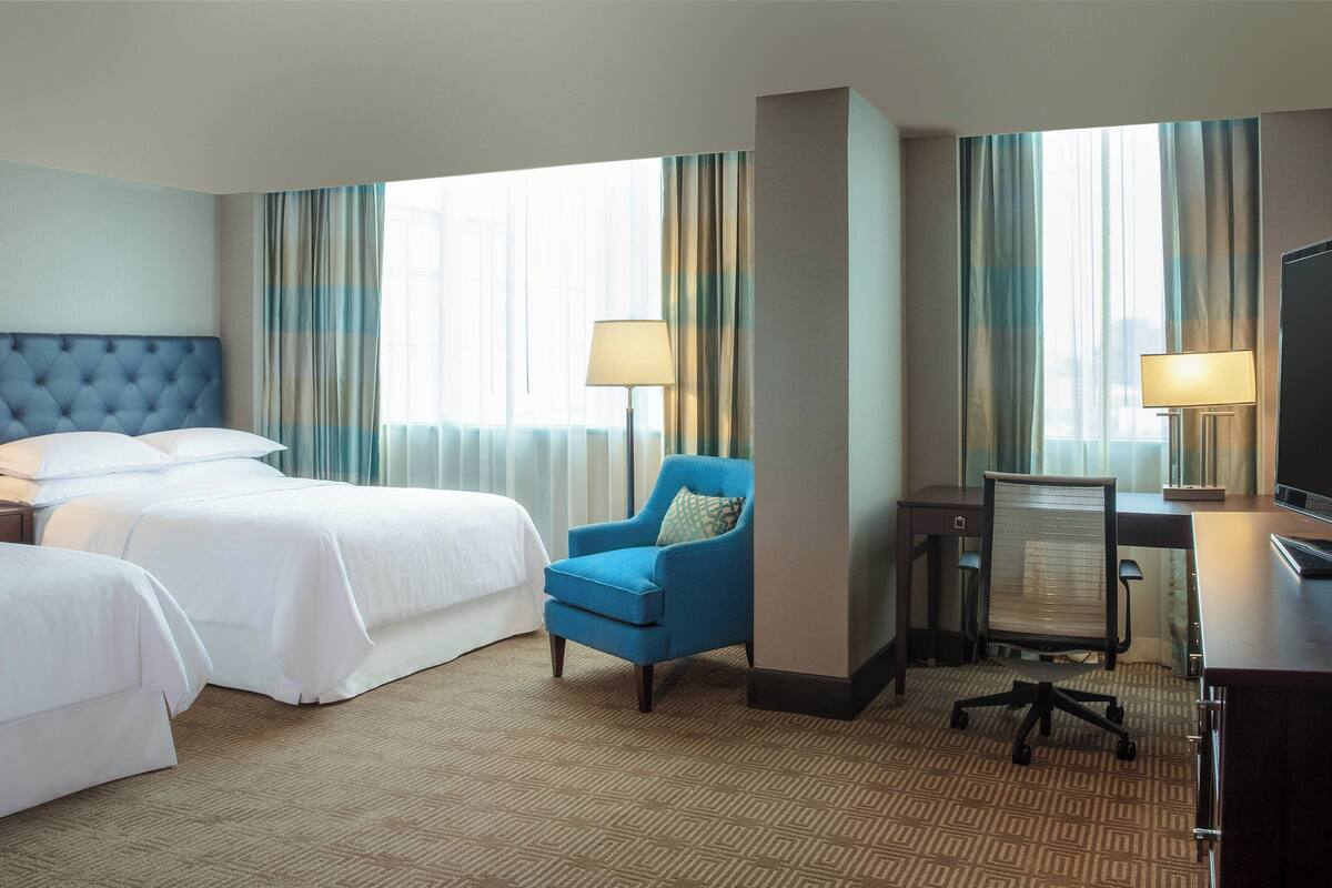 Una habitación de hotel con dos camas, un sillón azul, un escritorio con una silla y un televisor.