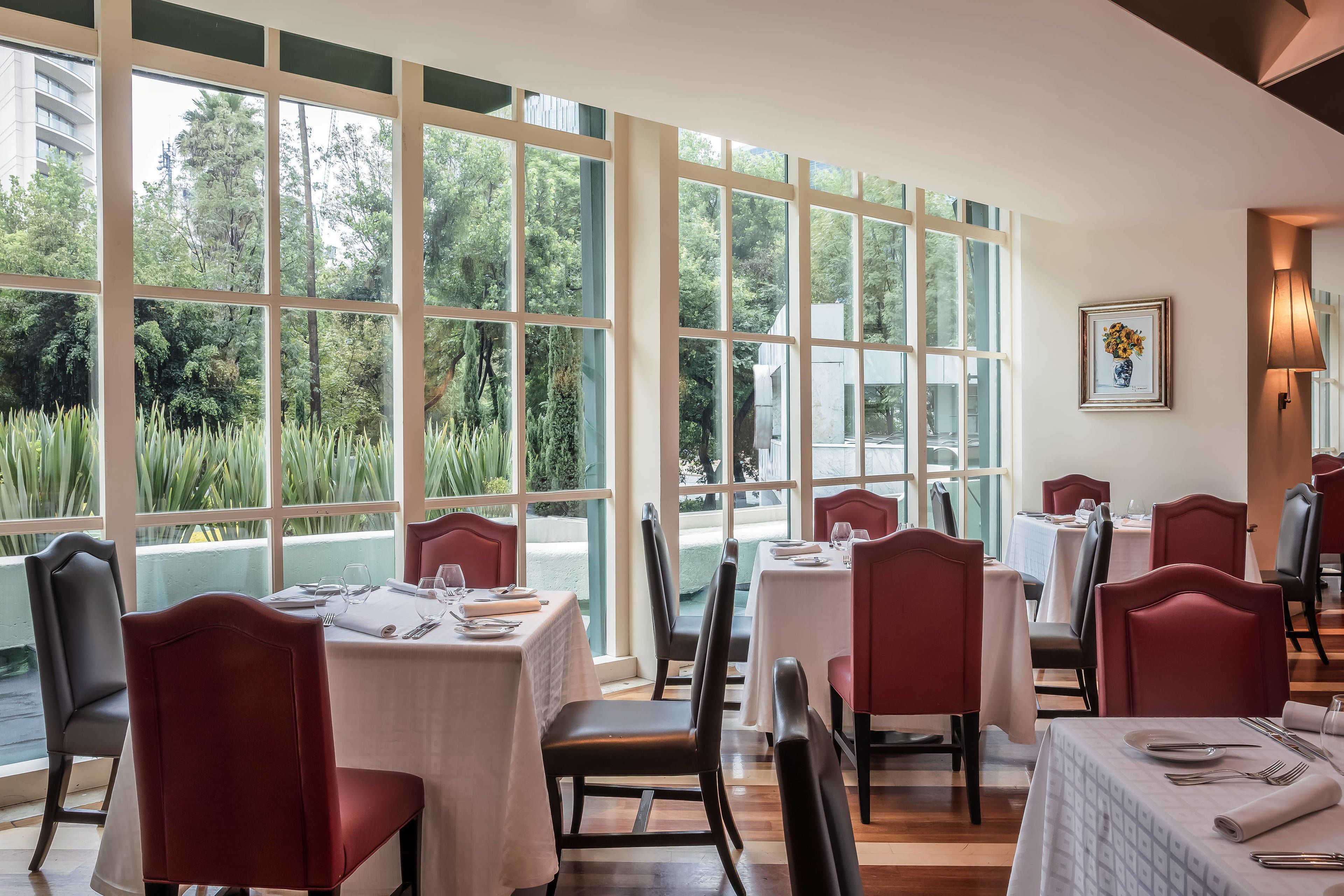 Ein Restaurant mit großen Fenstern, Tischen mit weißen Tischdecken und roten Stühlen.