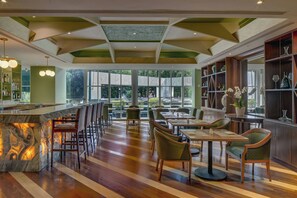 A spacious restaurant with a marble bar, wooden flooring, and a view of the outdoors.