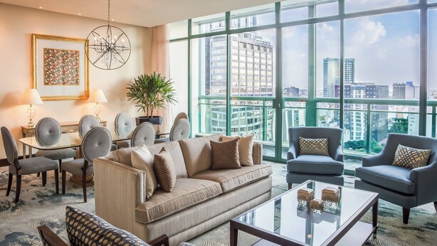 A spacious living room with a large window offering a city view, a dining area with a table and chairs, and a comfortable seating arrangement.