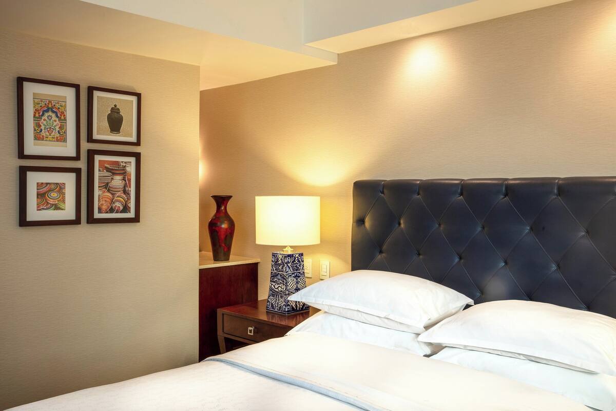 A hotel room with a bed, a nightstand, a lamp, and framed artwork on the wall.