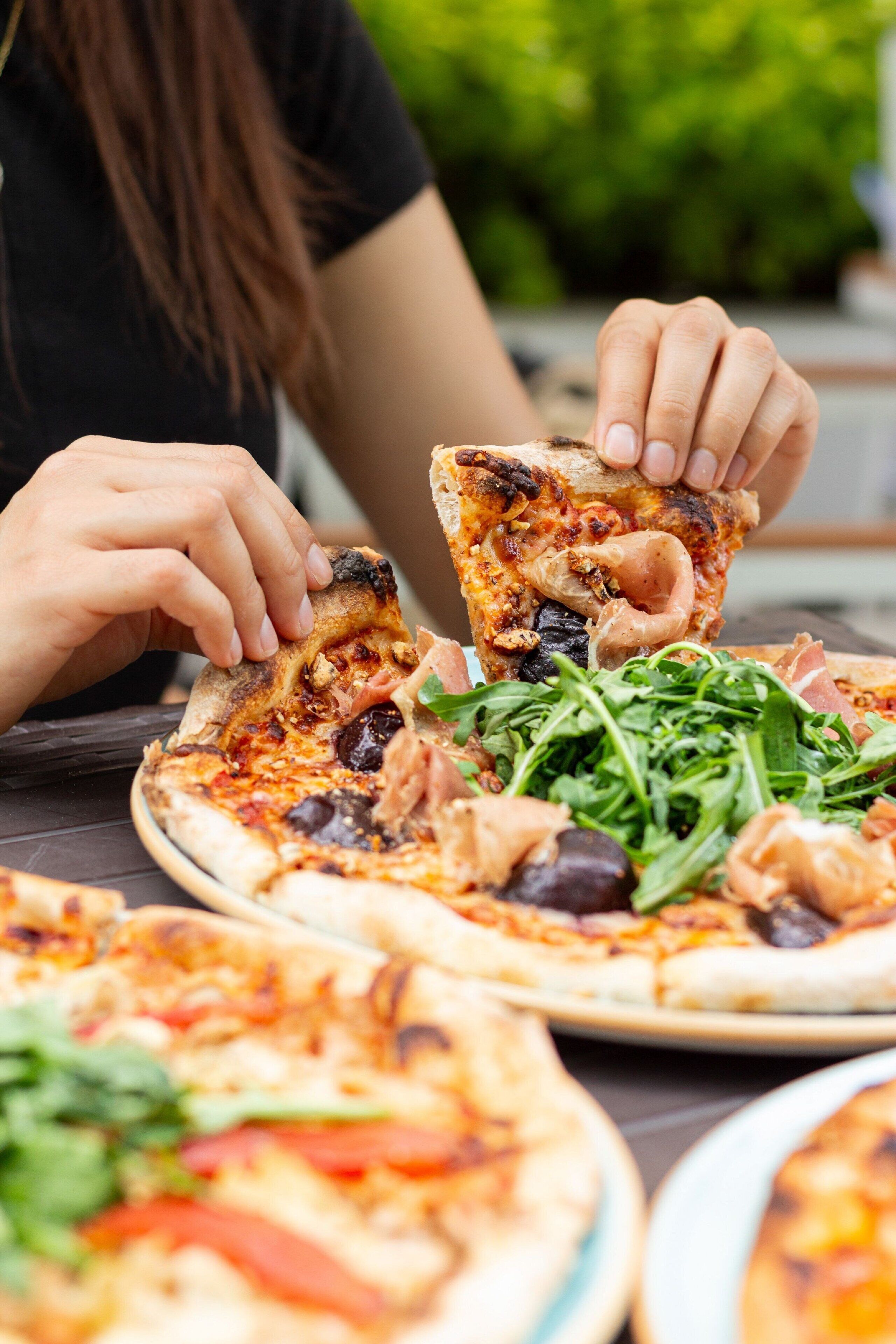 Una persona sosteniendo una porción de pizza con ingredientes visibles como aceitunas, queso y vegetales.