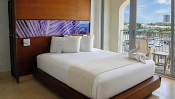 Habitación de hotel con una cama grande, cabecera de madera, vista de la ciudad desde un balcón y un cuadro sobre la cama.