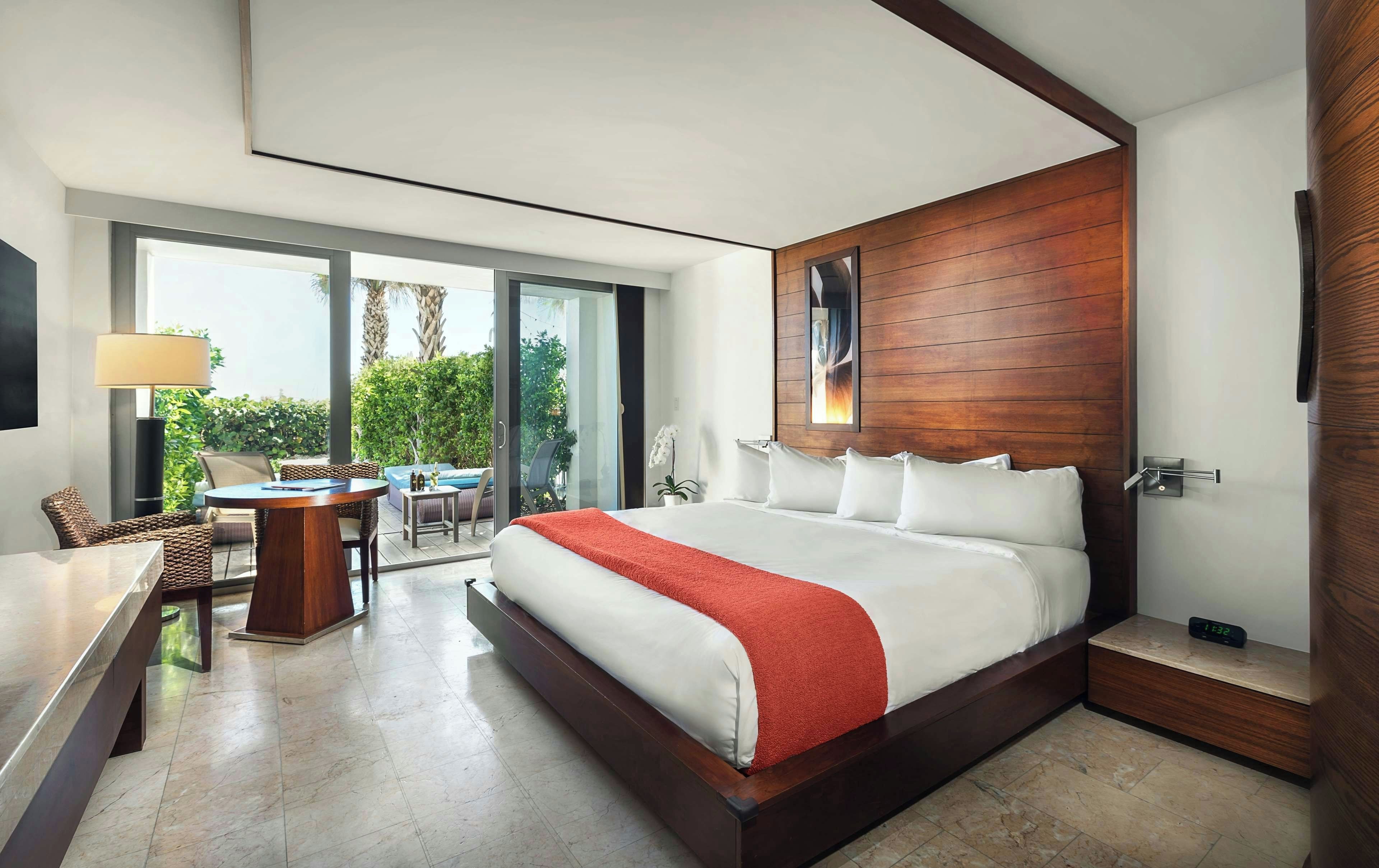 A modern hotel room with a large bed, a desk, and a view of the outdoors.