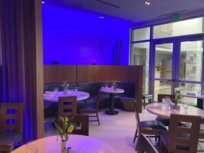 A restaurant interior with round tables, chairs, and a blue-lit wall. - Costa d'Este Beach Resort and Spa (Vero Beach)