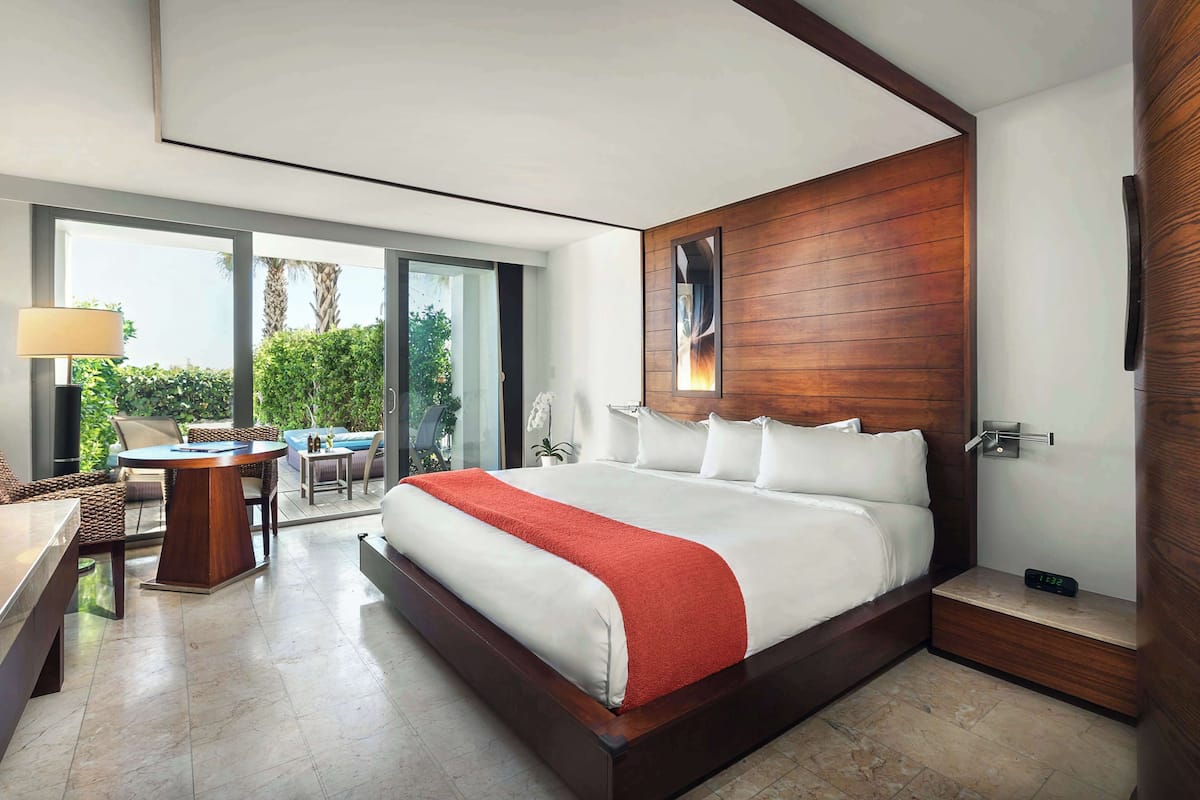 A modern hotel room with a large bed, a desk, and a balcony with outdoor furniture.