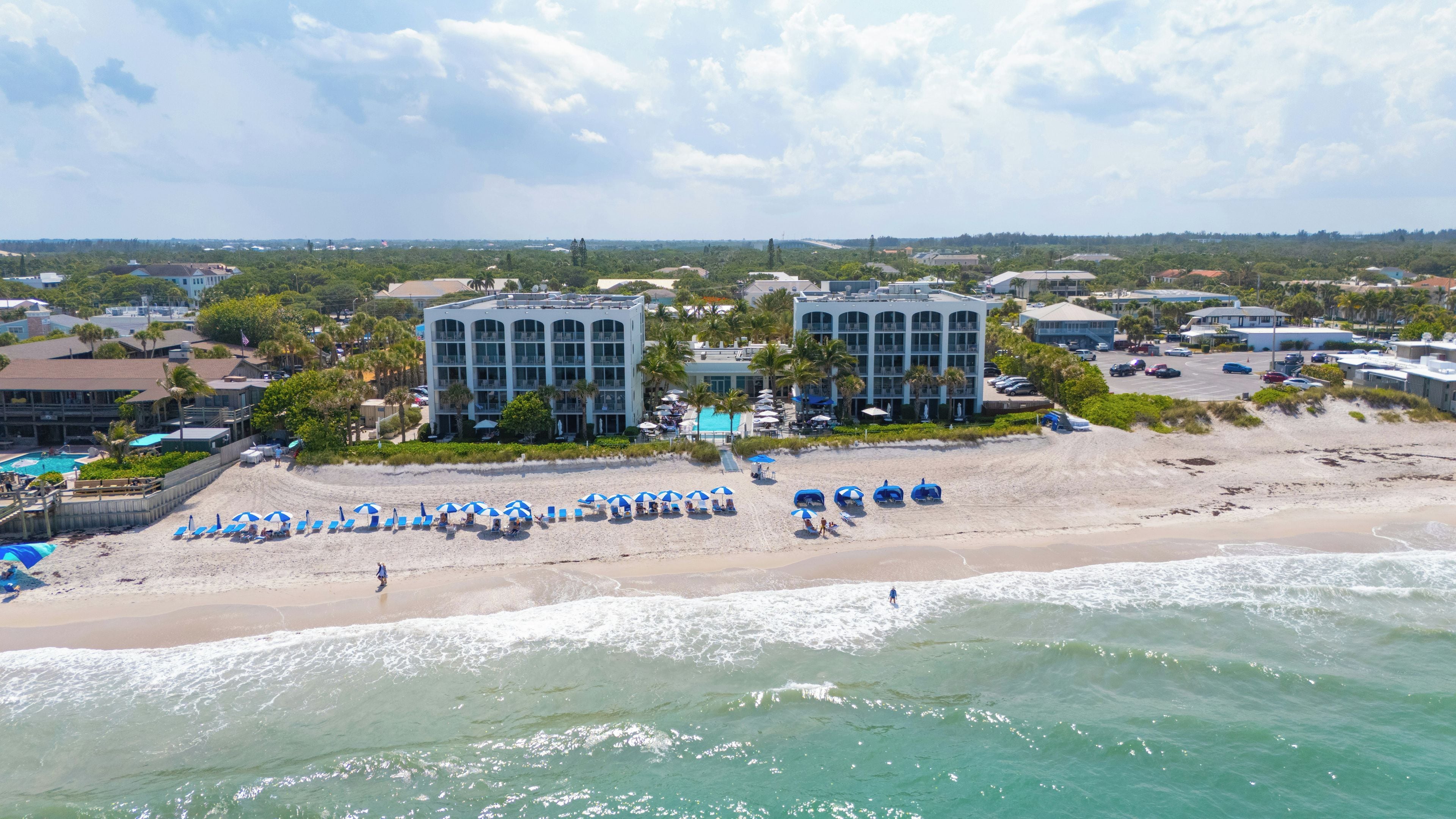 A beachfront hotel with multiple buildings, a sandy beach, and a pool area.