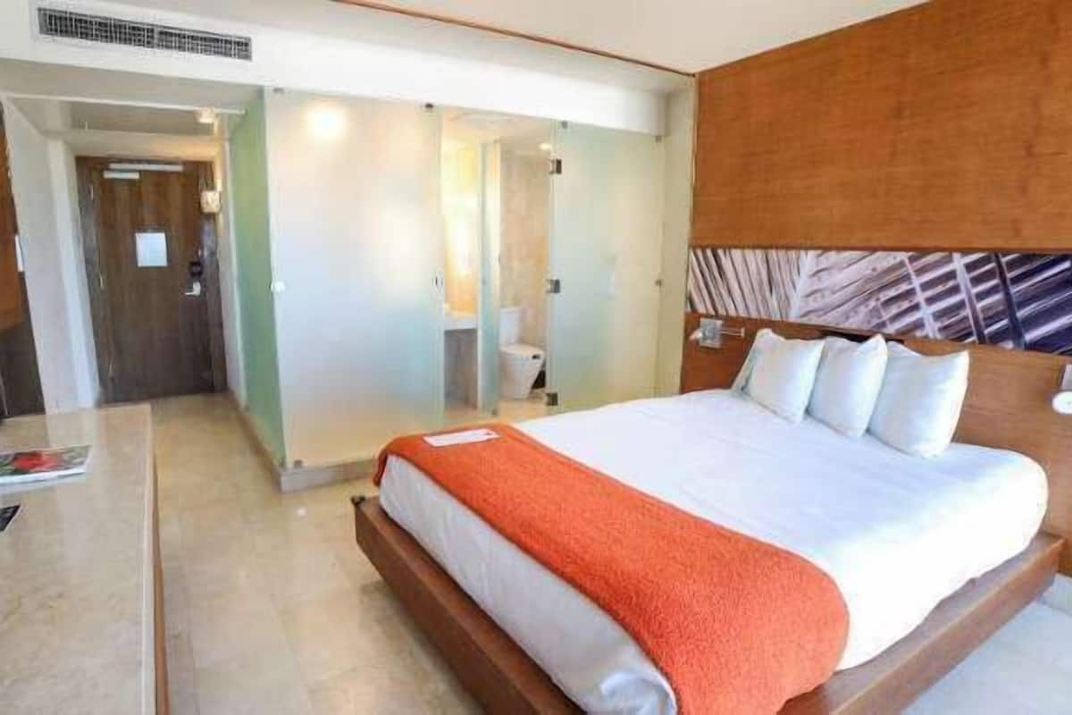 A hotel room with a large bed, a wooden headboard, a bedside table, and a mirror.