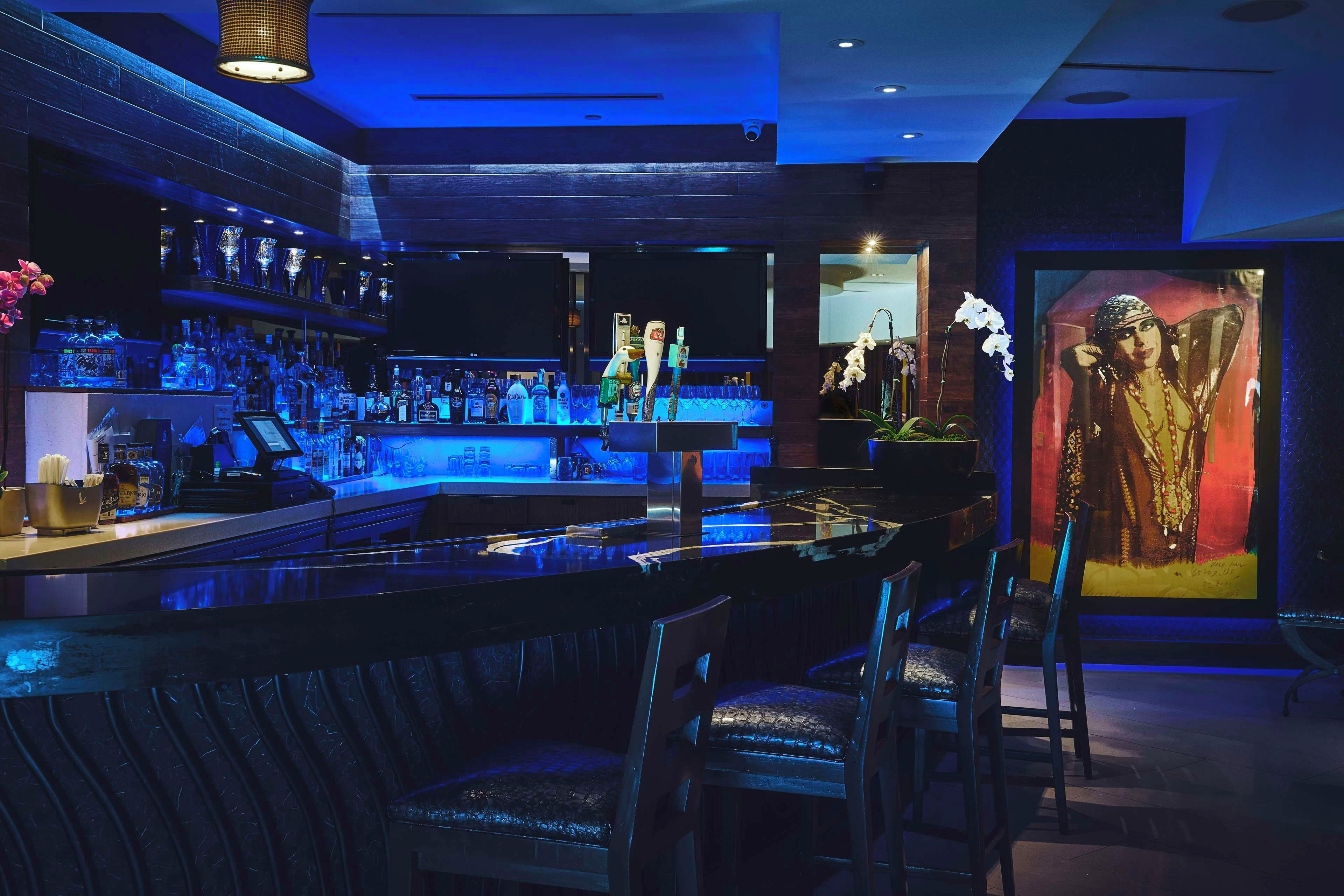 Eine Bar mit einer Theke, Sitzgelegenheiten und einem großen gerahmten Kunstwerk an der Wand.