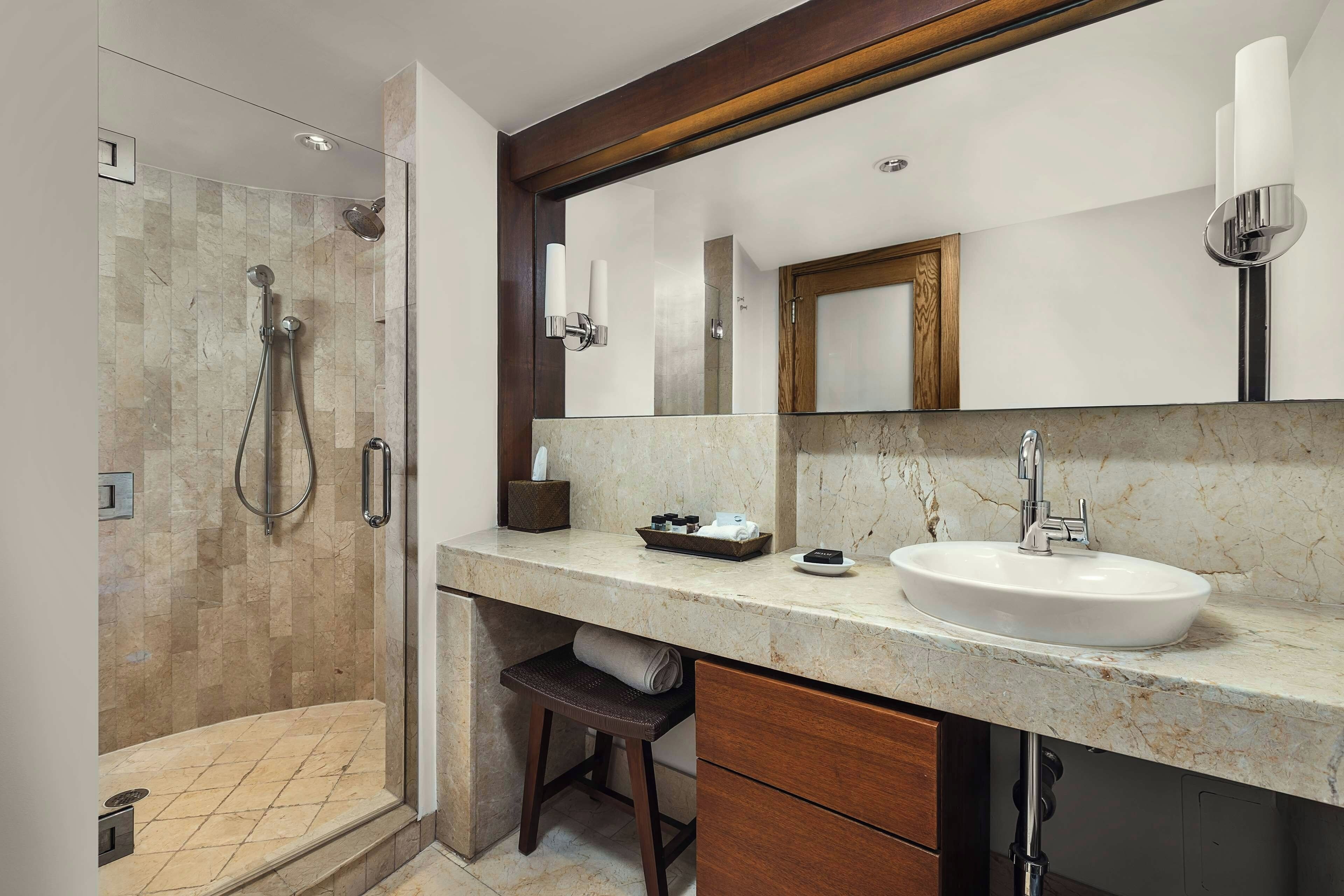 A modern bathroom with a glass-enclosed shower, a marble countertop, a sink, and a large mirror.