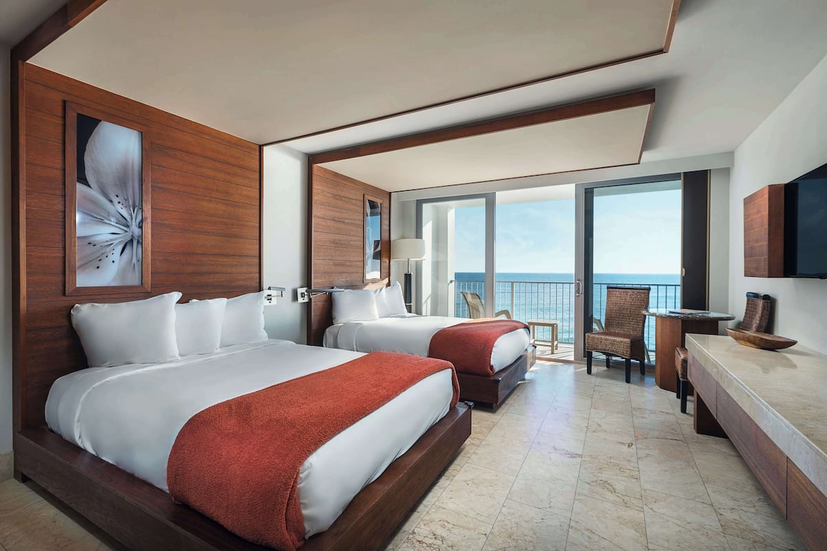 A hotel room with two beds, a balcony with a view, a desk, and a chair.