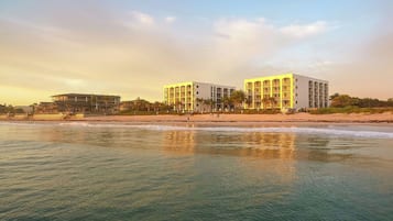 Un hotel sulla spiaggia con diversi edifici, una spiaggia sabbiosa e l'oceano.