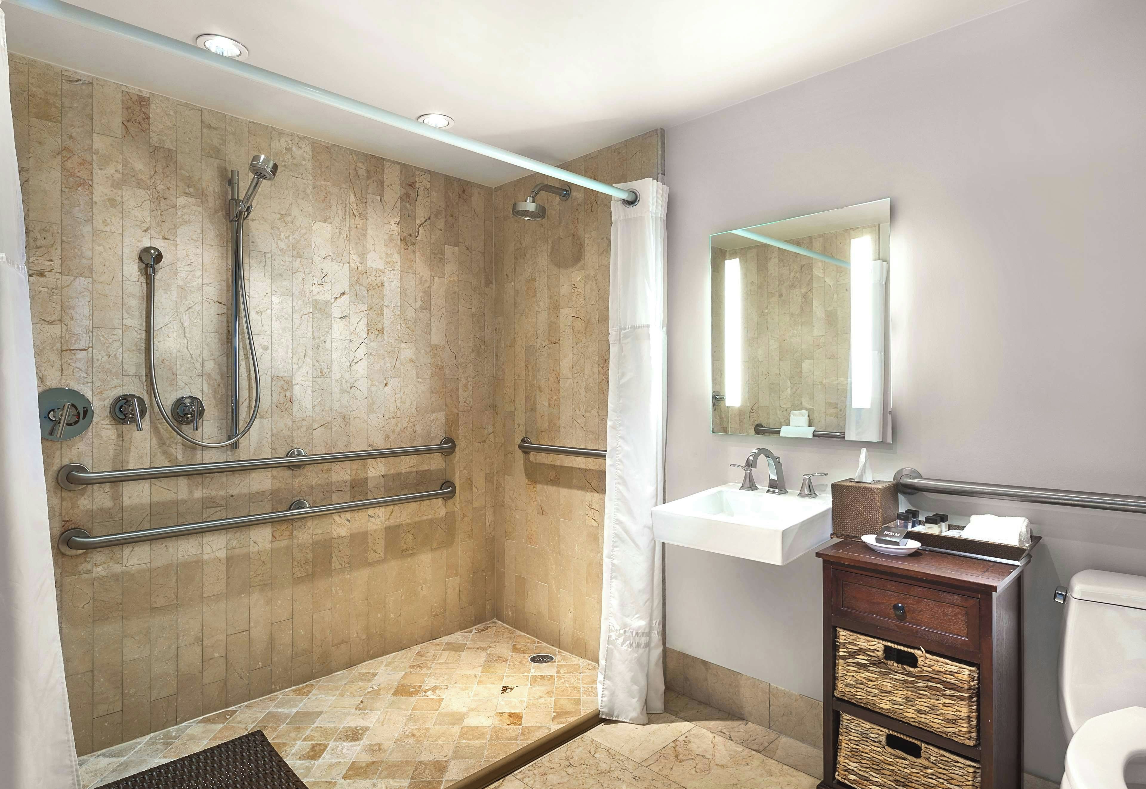 A modern bathroom with a walk-in shower, grab bars, a sink with a mirror, and a toilet.
