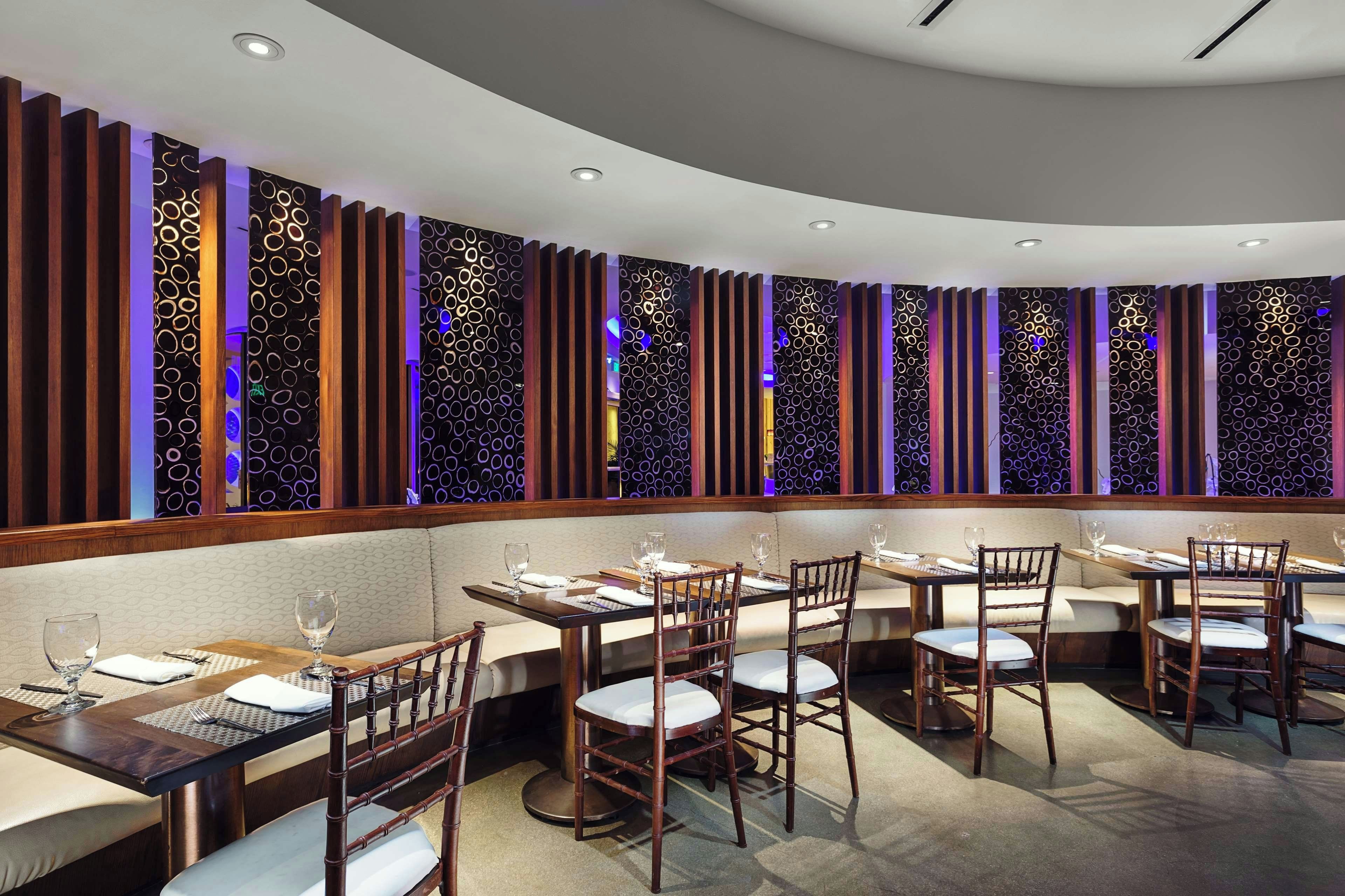 A restaurant with multiple tables and chairs, a patterned wall design, and recessed ceiling lighting.