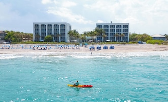 Una playa con un kayakista, sombrillas y dos edificios grandes al fondo.