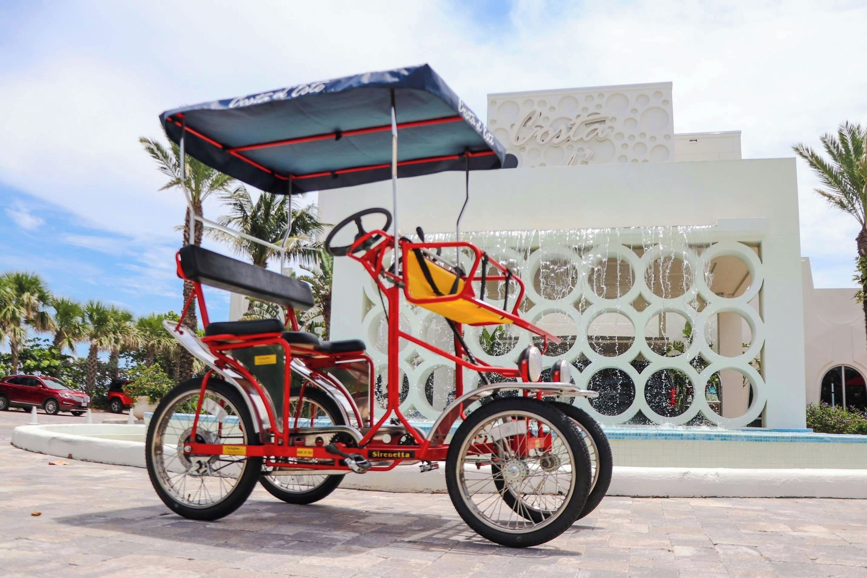 A red three-wheeled vehicle with a canopy, parked in front of a building with a decorative wall.