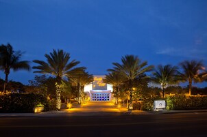 Entrada de hotel al anochecer, con palmeras y señalización iluminada.