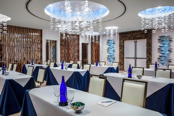 Une salle de conférence équipée de tables rondes, de chaises et d’un lustre moderne.