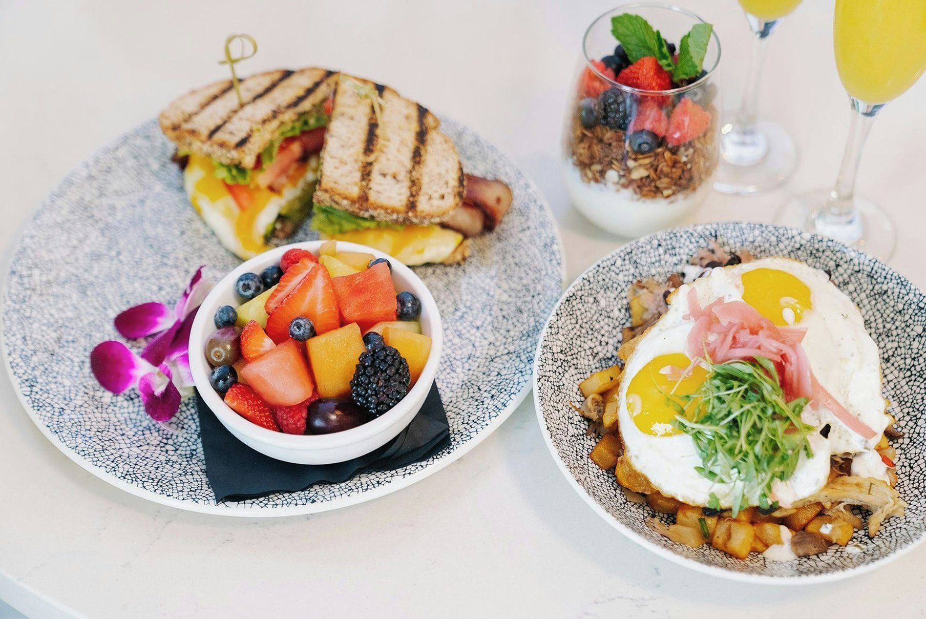 A breakfast setting with a sandwich, fruit bowl, and a plate with eggs and potatoes.