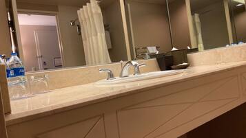 A bathroom with a large mirror, a sink, and a glass of water on the counter.