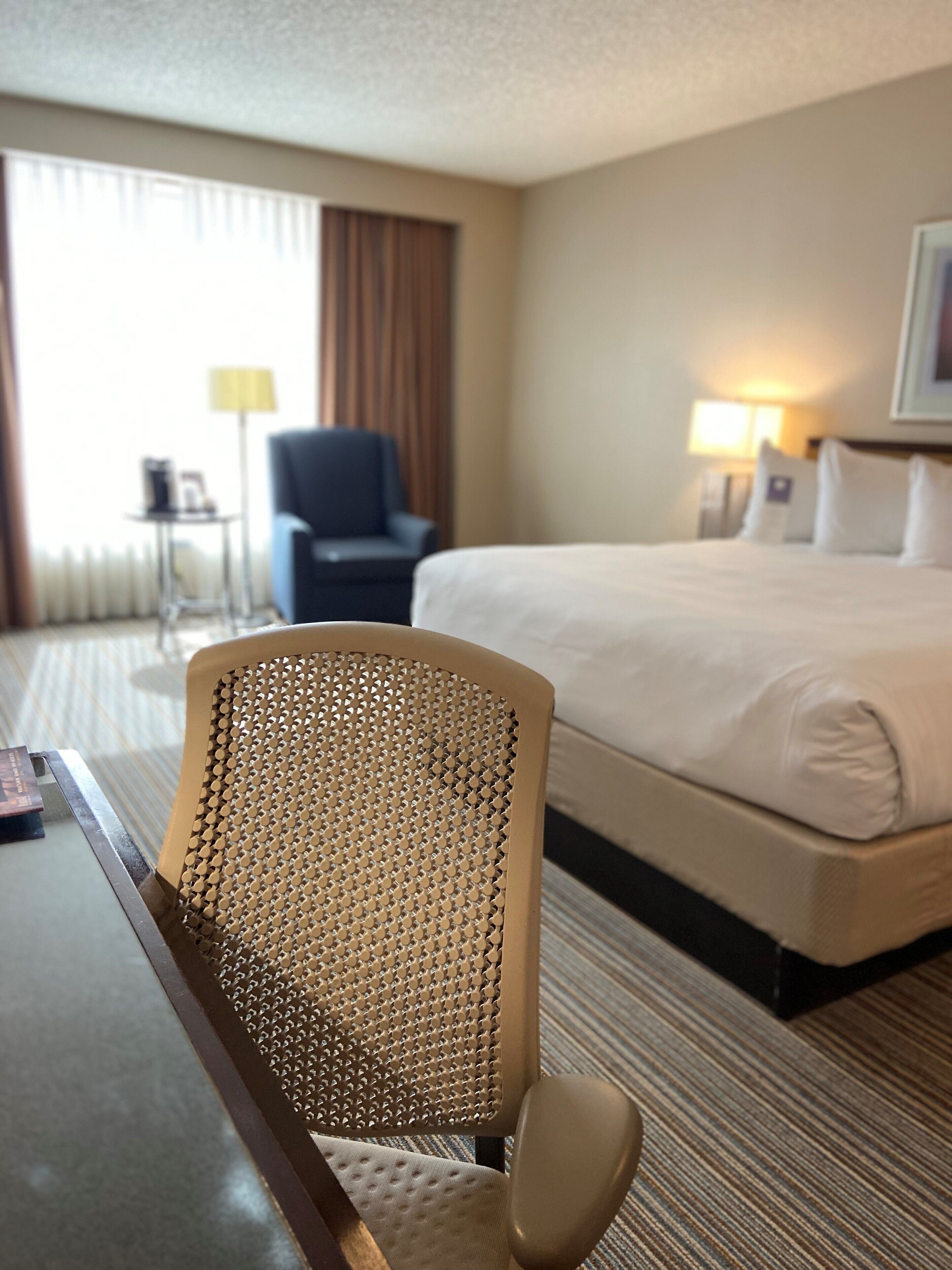 A hotel room with a bed, a chair, a desk, and a lamp.