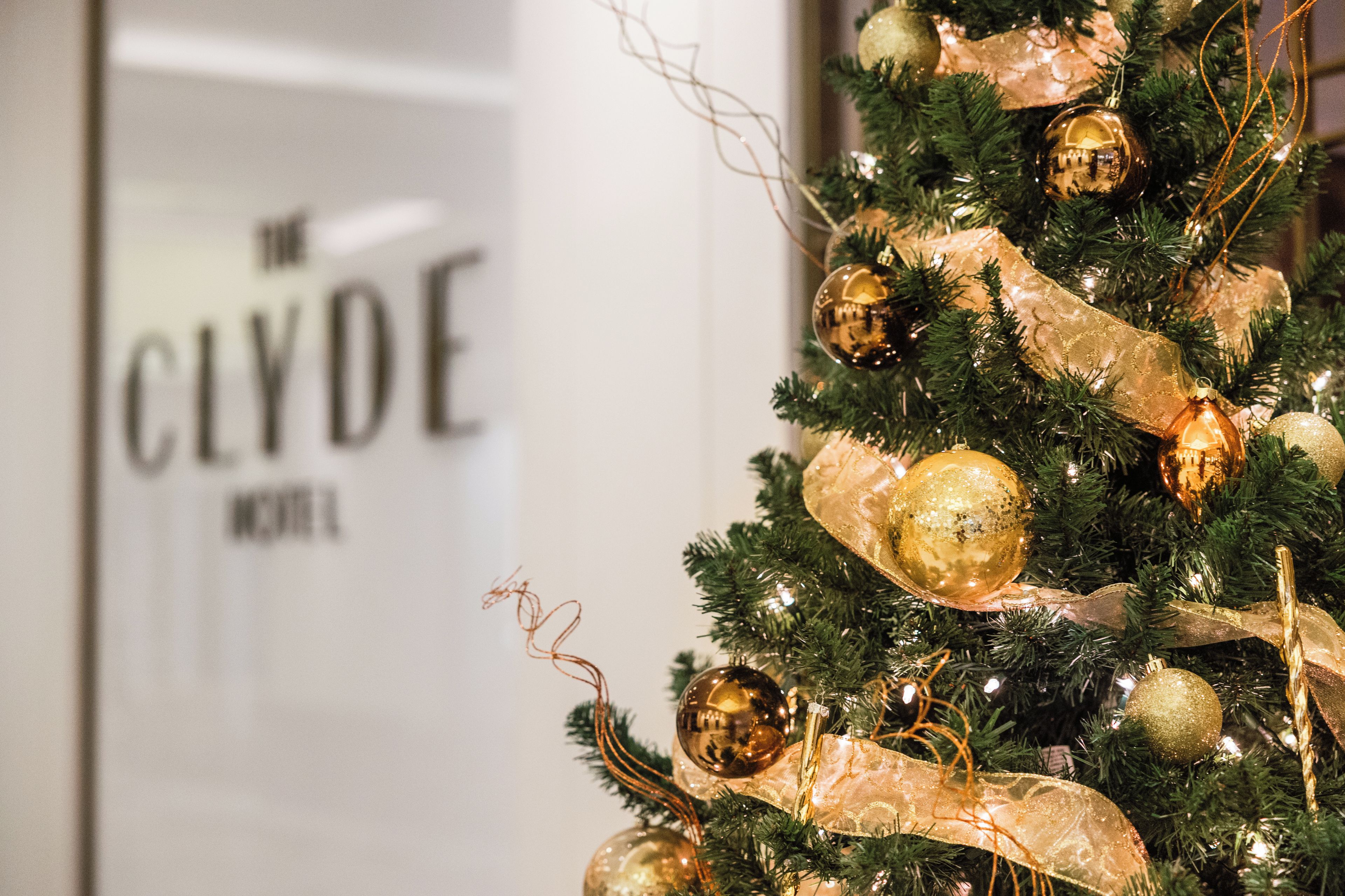 A Christmas tree with ornaments and a ribbon, with a blurred background featuring a sign.
