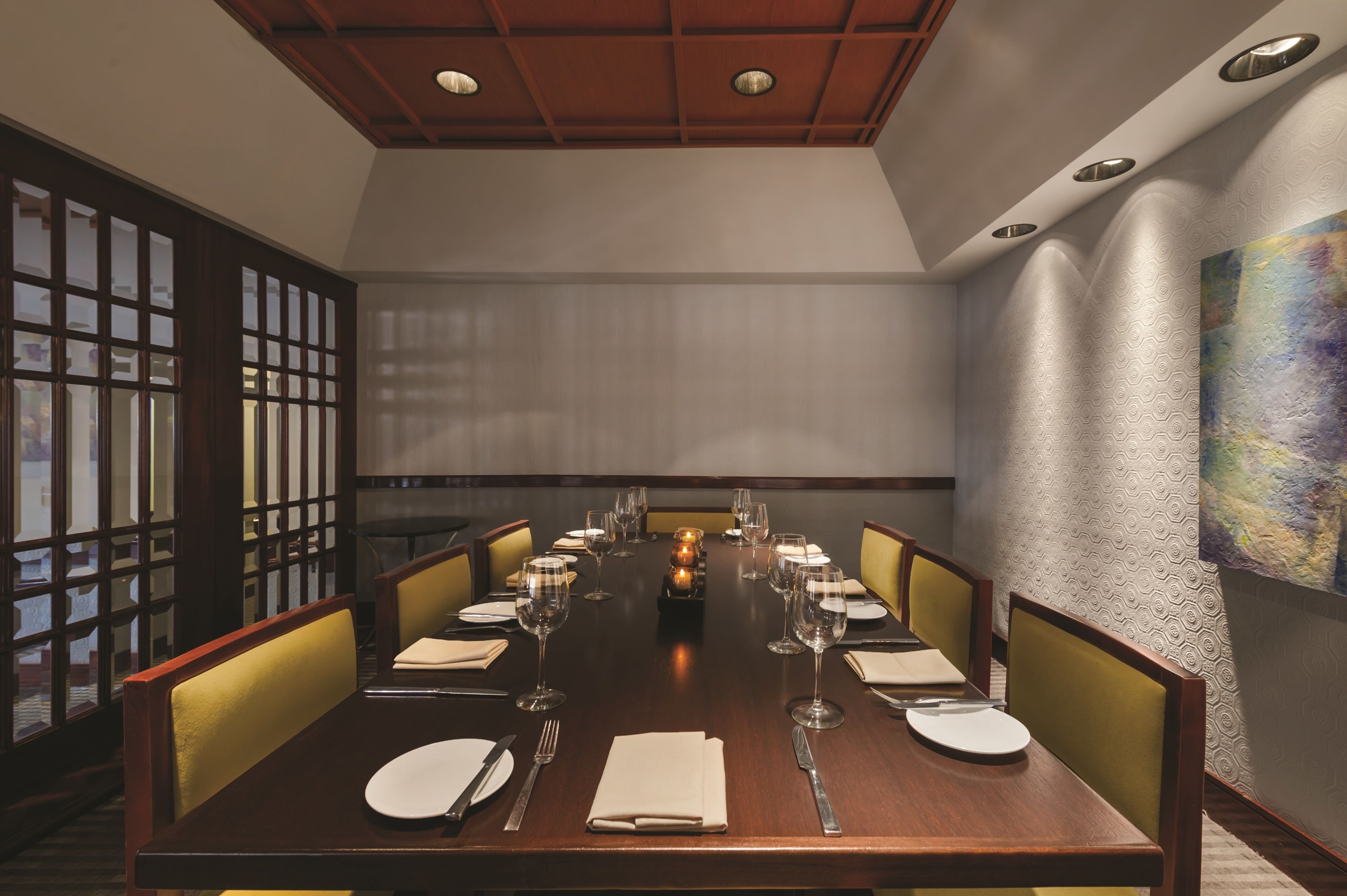 A dining room with a long table set for a meal, featuring chairs, plates, cutlery, and glasses.