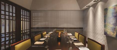 A dining room with a long table set for a meal, featuring chairs, plates, cutlery, and glasses.