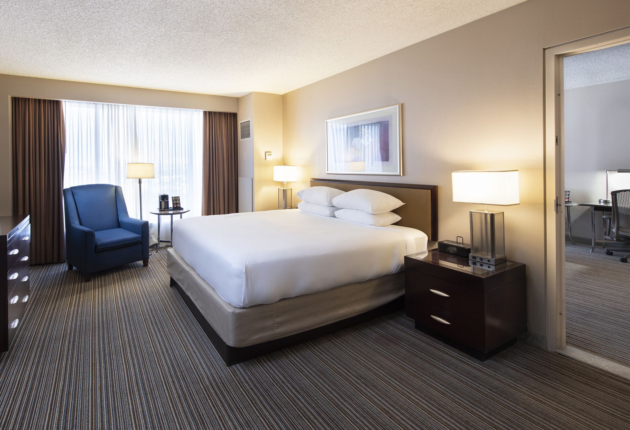 A hotel room with a large bed, a chair, two bedside tables with lamps, and a mirror.