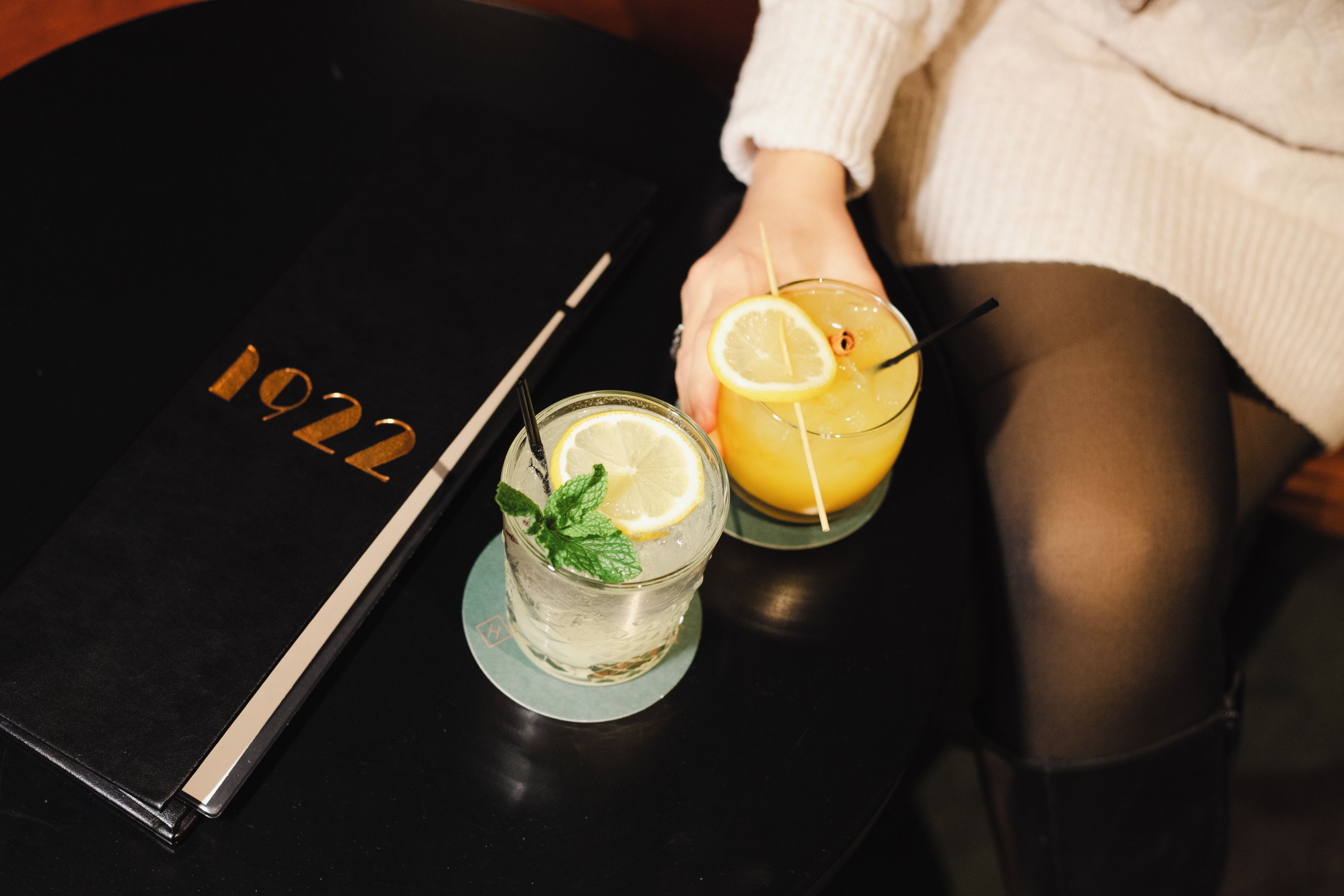 A table with a menu, two glasses of a yellow beverage, and a black notebook with the year '1922' on it.