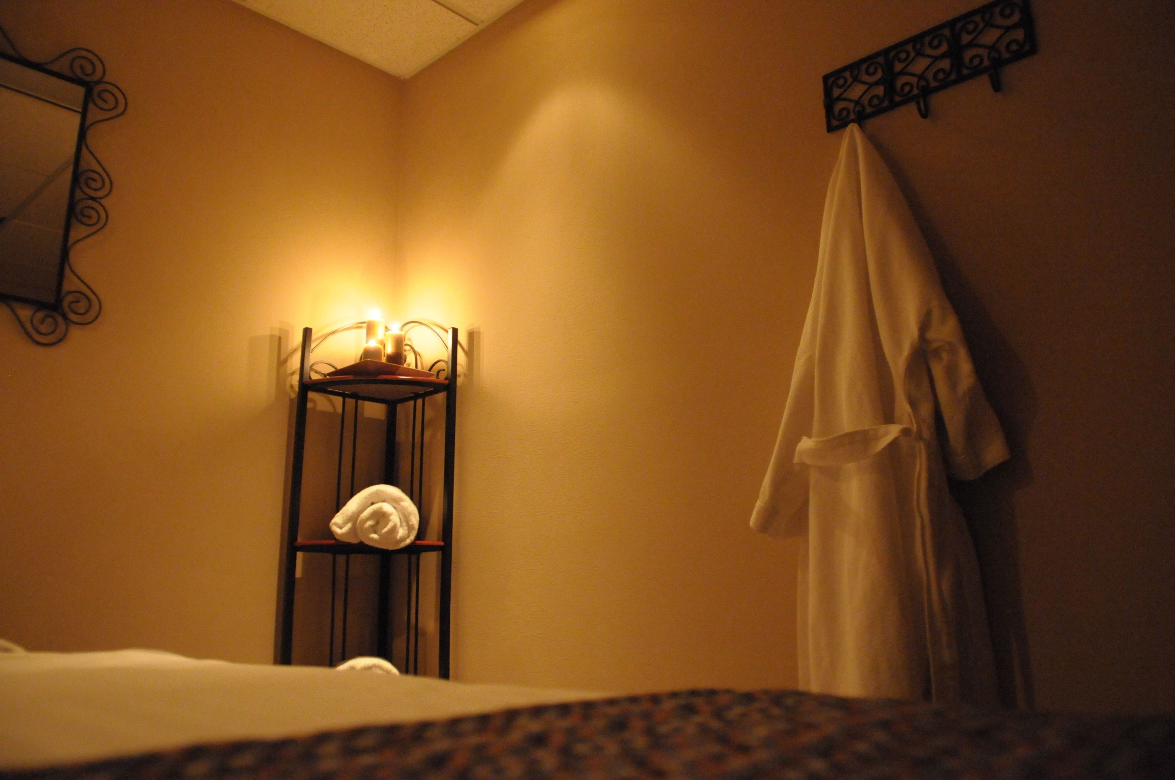 A hotel room with a bed, a bedside table with a lamp, a robe hanging on the wall, and a towel on the table.